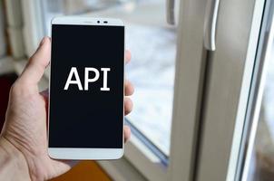 A person sees a white inscription on a black smartphone display that holds in his hand. API photo