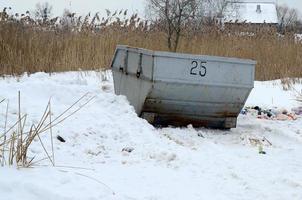 Trash bin at the side of street in winter with lip garbage container winter snow. Metal container for household waste photo