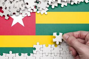 Togo flag is depicted on a table on which the human hand folds a puzzle of white color photo
