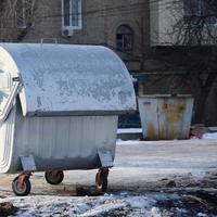 A silver garbage container stands near residential buildings in winter photo