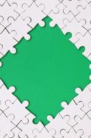 Framing in the form of a rhombus, made of a white jigsaw puzzle around the green space photo
