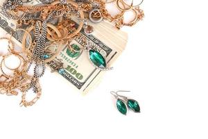 muchos costosos anillos, aretes y collares de joyería de oro y plata con una gran cantidad de billetes de dólares estadounidenses sobre fondo blanco. casa de empeño o joyería foto