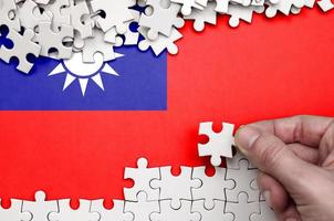 Taiwan flag is depicted on a table on which the human hand folds a puzzle of white color photo