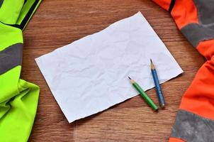 A crumpled sheet of paper with two pencils surrounded by green a photo