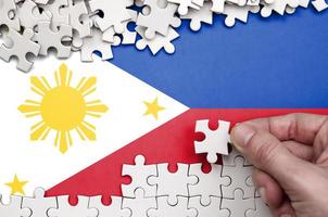 Philippines flag is depicted on a table on which the human hand folds a puzzle of white color photo