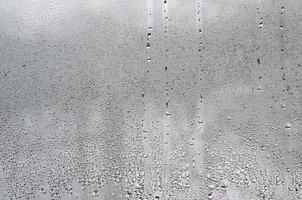 textura de una gota de lluvia sobre un fondo transparente húmedo de vidrio. tonificado en color gris foto