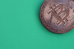 Chocolate product in the form of physical bitcoin lies on a green plastic background. Model of the crypto currency in the edible form photo