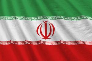 Iran flag with big folds waving close up under the studio light indoors. The official symbols and colors in banner photo