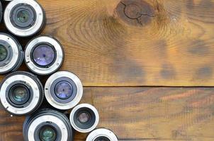 Several photographic lenses lie on a brown wooden background. Space for text photo