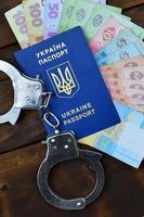 A photograph of a Ukrainian foreign passport, a certain amount of Ukrainian money and police handcuffs. Concept of illegal earnings of Ukrainian citizens abroad photo