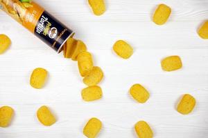 KHARKOV, UKRAINE - MAY 3, 2022 Pringles el nacho cheese flavour. Cardboard tube can with Pringles potato chips on white table. Pringles is a brand of snack chips owned by Kellogg Company photo