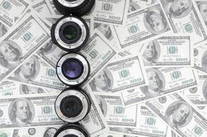 A few photographic lenses lies on the background of a lot of dollar bills. Space for text photo