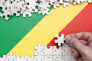 Congo flag is depicted on a table on which the human hand folds a puzzle of white color photo