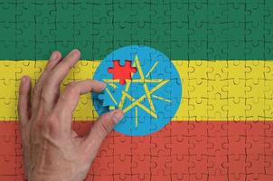Ethiopia flag is depicted on a puzzle, which the man's hand completes to fold photo