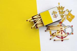 Vatican City State flag is shown on an open matchbox, from which several matches fall and lies on a large flag photo