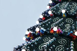 A fragment of a huge Christmas tree with many ornaments, gift boxes and luminous lamps. Photo of a decorated Christmas tree close-up with copy space