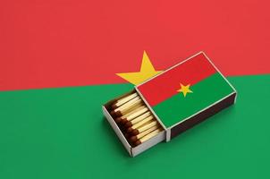 Burkina Faso flag is shown in an open matchbox, which is filled with matches and lies on a large flag photo