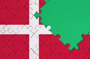 Denmark flag is depicted on a completed jigsaw puzzle with free green copy space on the right side photo