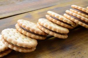 A round sandwich cookie with coconut filling lies in large quantities on a brown wooden surface. Photo of edible treats on a wooden background with copy space