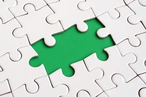 Close-up texture of a white jigsaw puzzle in assembled state with missing elements forming a green pad for text. Copy space photo