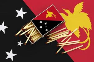 Papua New Guinea flag is shown on an open matchbox, from which several matches fall and lies on a large flag photo