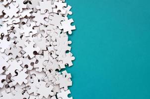 A pile of uncombed elements of a white jigsaw puzzle lies on the background of a blue surface. Texture photo with copy space for text