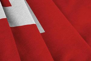 Tonga flag with big folds waving close up under the studio light indoors. The official symbols and colors in banner photo