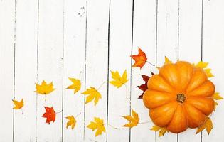 Thanksgiving background. Pumpkins and fallen leaves on white wooden background.  Halloween or Thanksgiving day or seasonal autumnal.  Flat lay. Top view photo