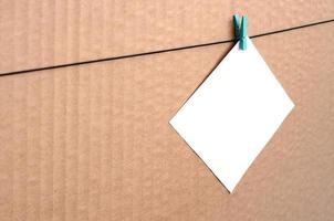 White blank card on rope on a brown cardboard background. Creative reminder, small sheet of paper on wooden clothespin, memo backdrop photo