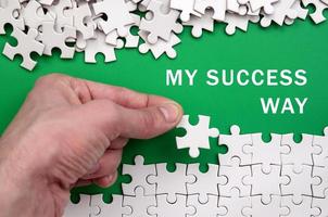 My success way. The hand folds a white jigsaw puzzle and a pile of uncombed puzzle pieces lies against the background of the green surface photo
