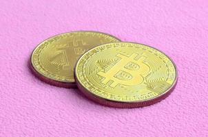 Two golden bitcoins lies on a blanket made of soft and fluffy light pink fleece fabric. Physical visualization of virtual crypto currency photo