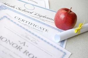 un reconocimiento del cuadro de honor, un certificado de logros y un diploma de escuela secundaria se encuentran en la mesa con un pequeño pergamino y una manzana roja. documentos educativos foto