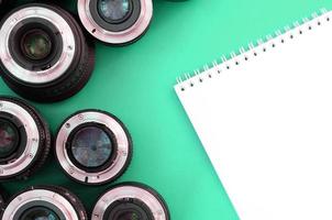 Several photographic lenses and white notebook lie on a bright turquoise background. Copy space photo