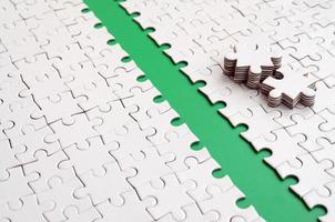 The green path is laid on the platform of a white folded jigsaw puzzle. The missing elements of the puzzle are stacked nearby. Texture image with space for text photo