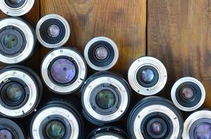 Several photographic lenses lie on a brown wooden background. Space for text photo