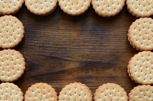 A frame of round cookie sandwich with coconut filling on a dark brown wooden surface. Unusual use of cookies as a frame. Image with copy space
