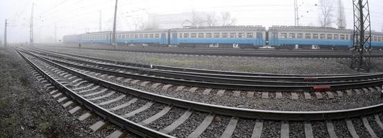 The Ukrainian suburban train rushes along the railway in a misty morning. Fisheye photo with increased distortion