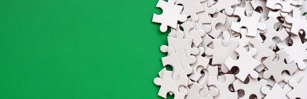 A pile of uncombed elements of a white jigsaw puzzle lies on the background of a green surface. Texture photo with copy space for text