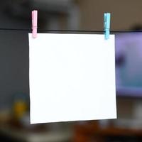 White blank card on rope, dark office background. Creative reminder, small sheet of paper on wooden clothespin, memo backdrop photo