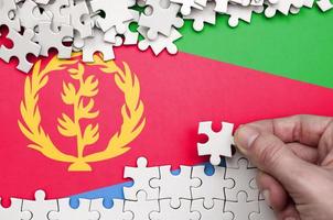 Eritrea flag is depicted on a table on which the human hand folds a puzzle of white color photo