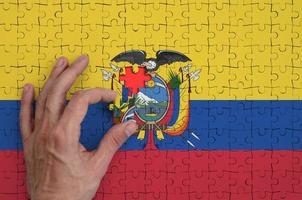 Ecuador flag is depicted on a puzzle, which the man's hand completes to fold photo