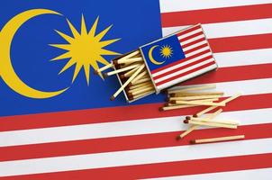 la bandera de malasia se muestra en una caja de cerillas abierta, de la que caen varias cerillas y se encuentra en una bandera grande foto