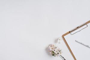 Clipboard and pen with white flowers of an apple tree on a white background. Flat lay and top view. Business concept. photo
