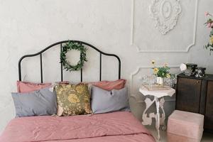 Bed with pink linens and gray pillows, a wreath of leaves on the bed photo