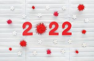 números rojos 2022 del año cortados de fieltro rojo sobre fondo de máscaras médicas azul claro con copos de nieve blancos de madera y pompones rojos. cero es un pompón esponjoso. revisión de los resultados del año coved-19. foto
