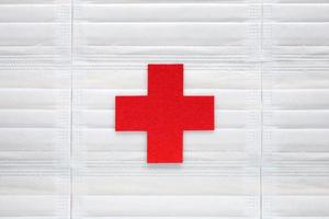 KRAKOW, POLAND, 2021 - Medical cross symbol cut out of red felt centered on light blue medical masks background. Healthcare system, medicine, humanitarian protection, assistance, medical aid. photo