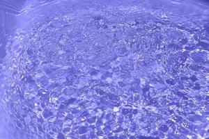 Defocus blurred transparent purple colored clear calm water surface texture with splash, bubble. Shining purple water ripple background. Surface of water in swimming pool. Purple bubble water shine. photo