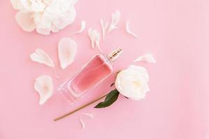 an elegant bottle of women's perfume or toilet water on a pink background with leaves and a peony bud. top view. a copy of the space. photo
