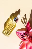 cosmetic bottle with a dropper on a beige background and flowers in the rays of the sun. a natural skin care product. vertical view. photo