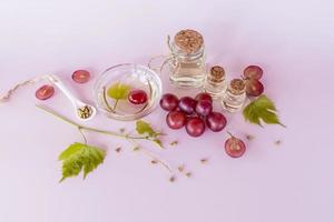 aceite de semilla de uva orgánico en una botella de vidrio con tapa de corcho, tazón, con uvas sobre un fondo rosa. cuidado de la piel del rostro. producción de colágeno. foto